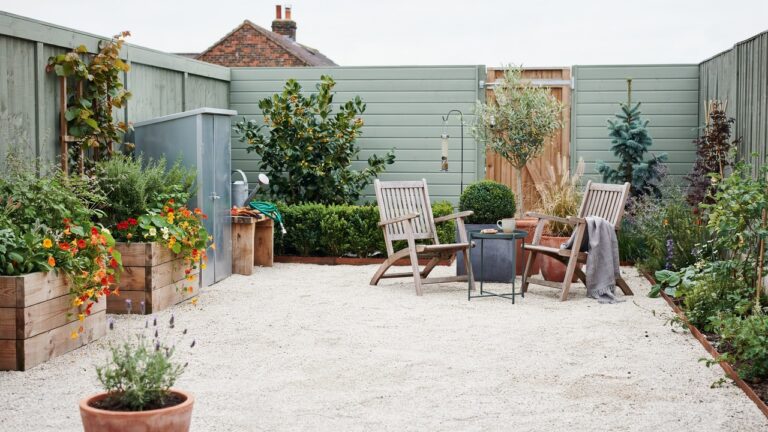 Low maintenance small UK garden with seating, gravel, raised beds, large planters and evergreen plants.